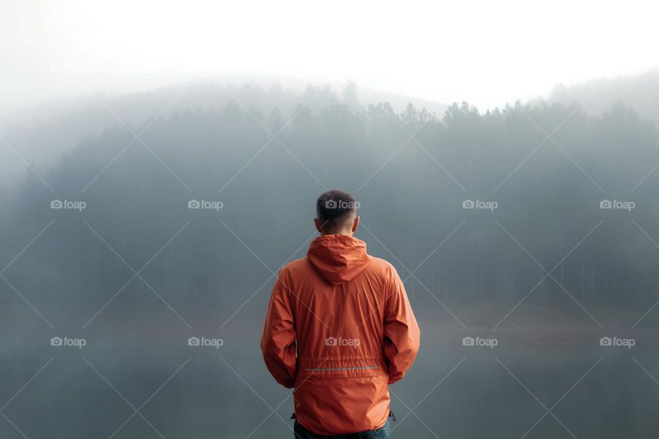 Rear view of man standing by the lake during mist 