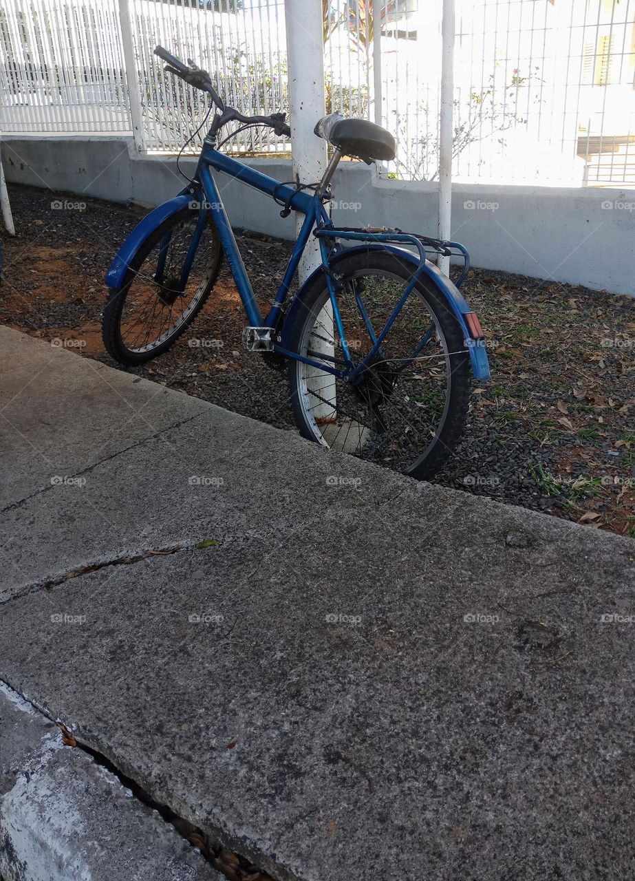 A blue bycicle locked at a white pole in a city
