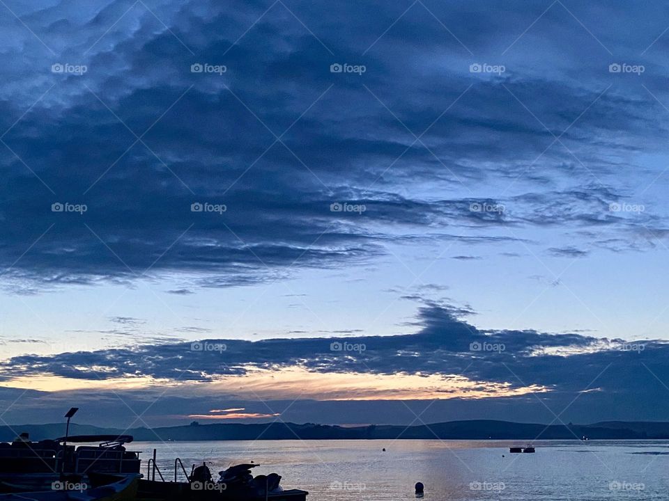 A serene scene with a body of water, boats in the foreground, and a dramatic, cloudy sky during dusk.