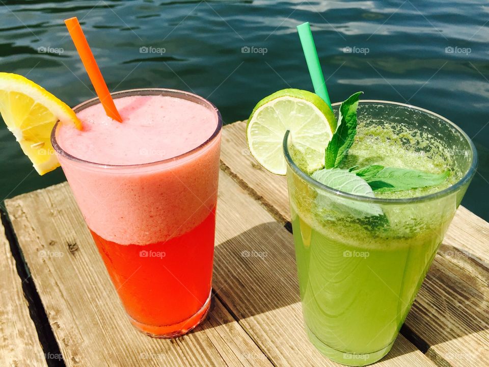 Strawberry lemonade and mint lemonade glasses near the lake