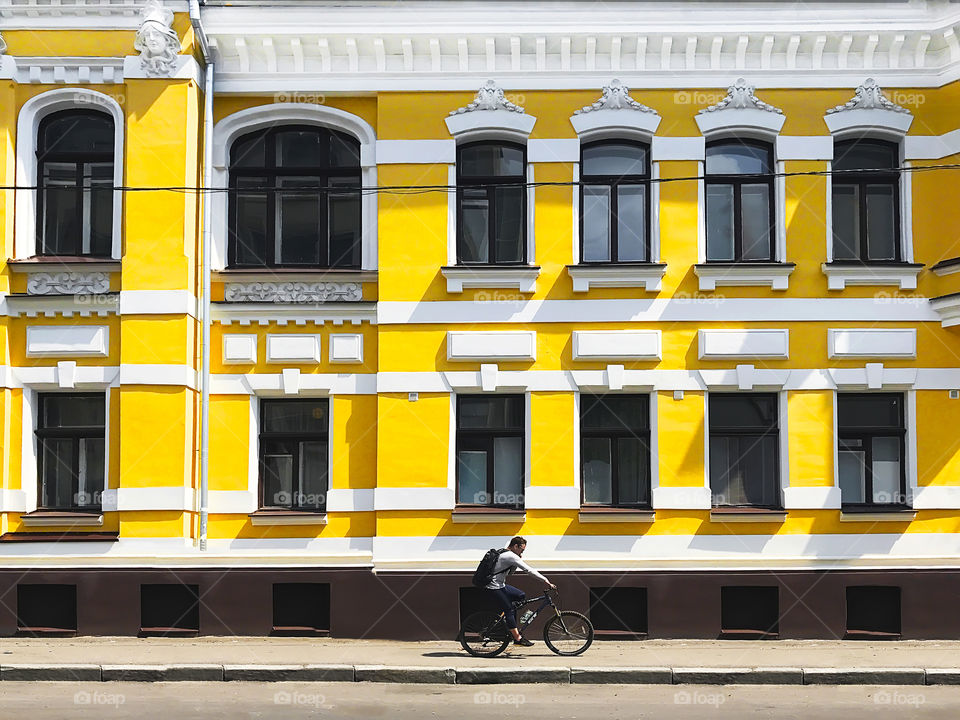 Cyclist riding a bicycle and using mobile phone in front of an old yellow and white building in the city 