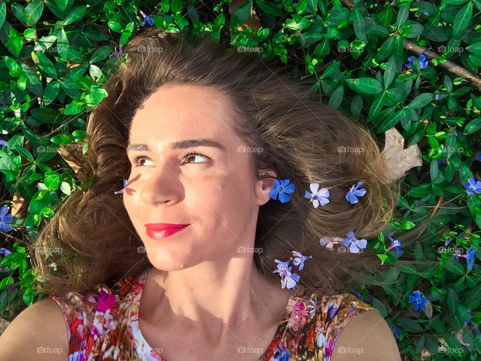 Portrait of young woman laying on grass with blue flowers in her hair