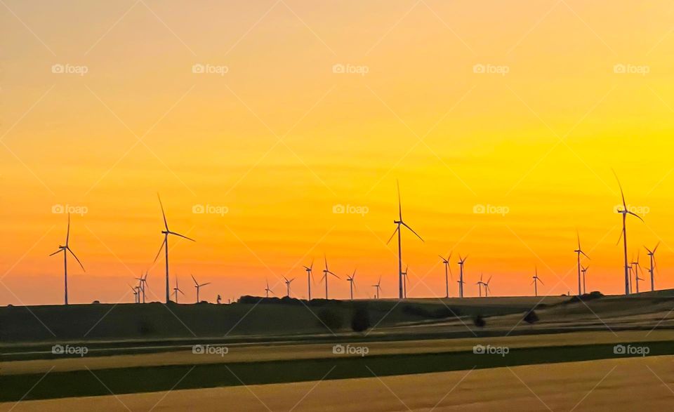 Scenic view of wind turbines on a field during vibrant sunset. Renewable energy landscape with colorful orange and yellow sky.
