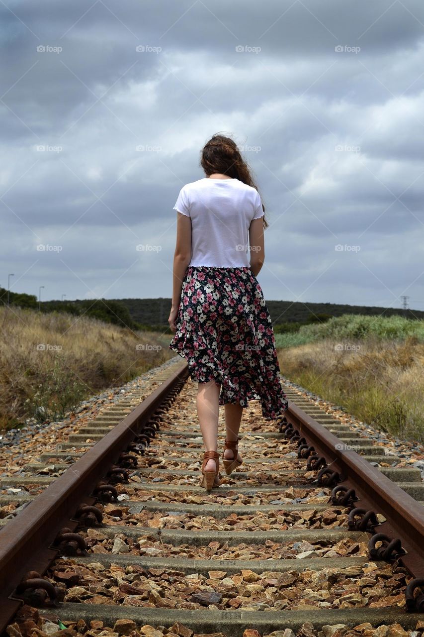 Railway walk on a rainy day with dark clouds in a floral skirt