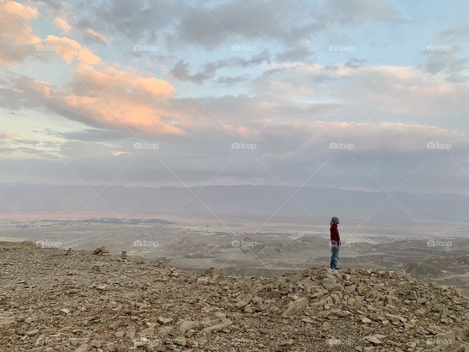 Man stand at the end of the cliff watching the view and changing colors of sunset