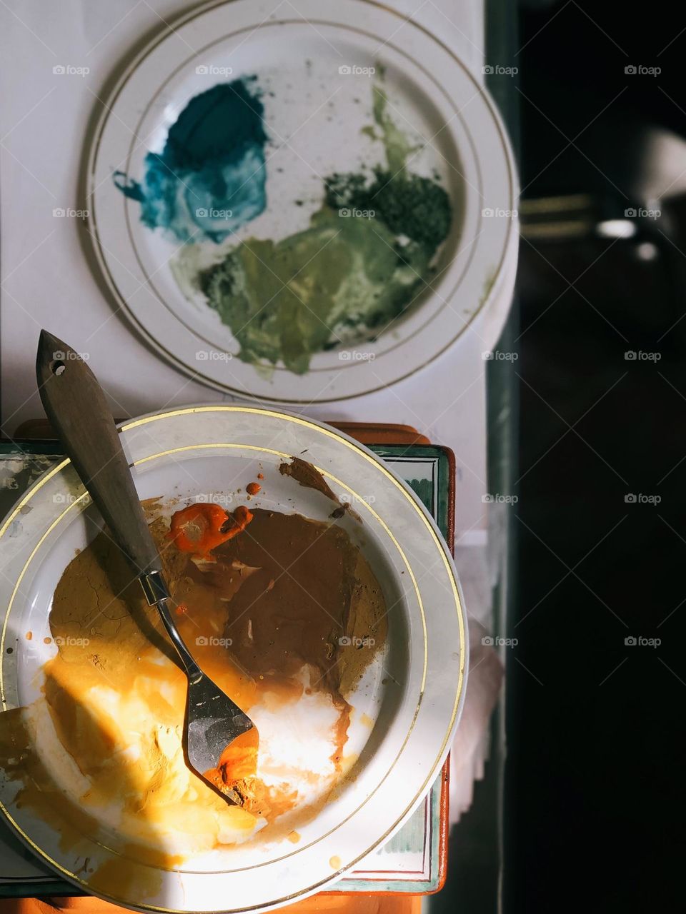 Two round porcelain plates with colored paint stand on the table in sunny day, no people 