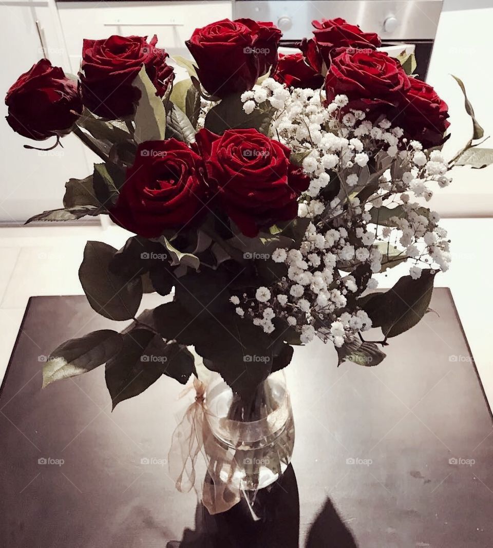 A beautiful bunch of red roses in a vase with a golden bow and white blossom