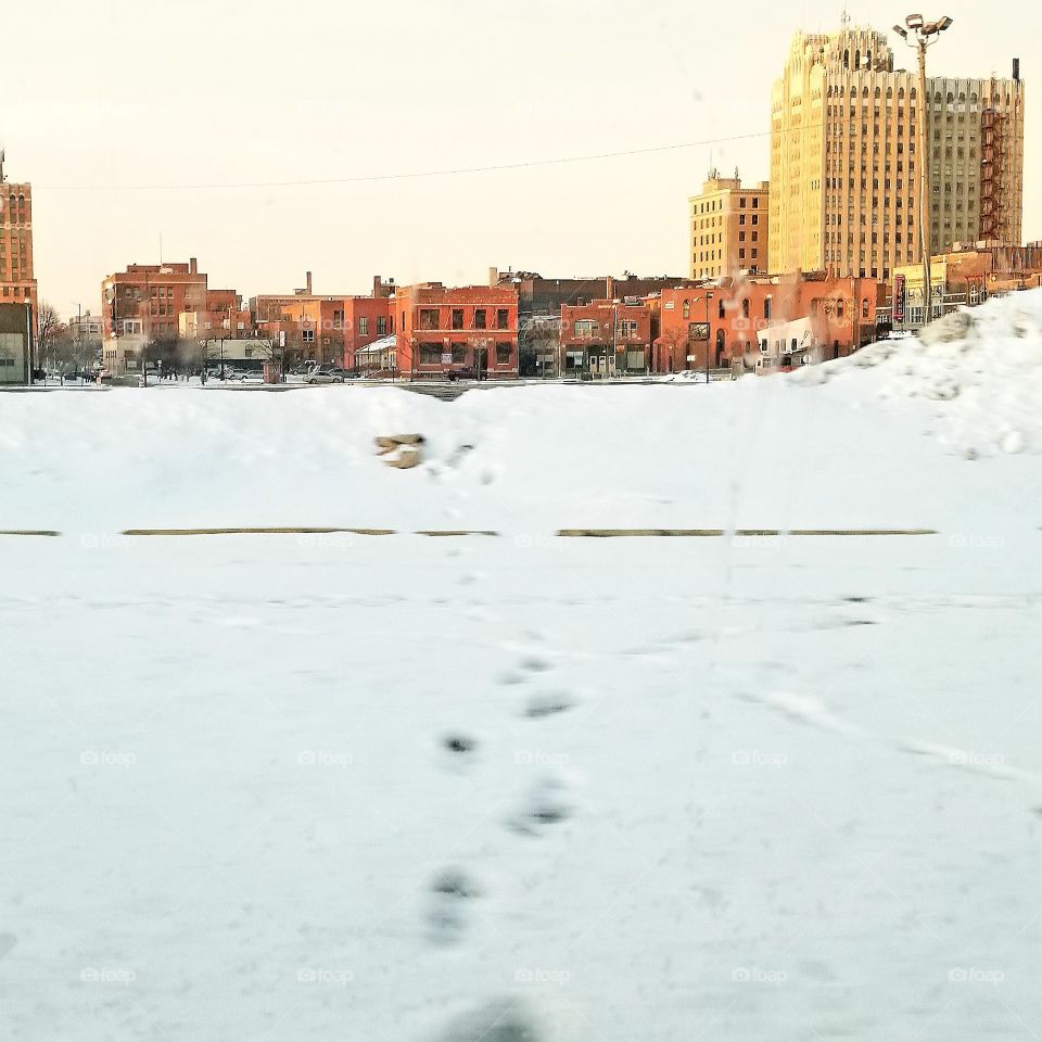 snowy footsteps going into the distance in downtown Pontiac, abandoned buildings in background