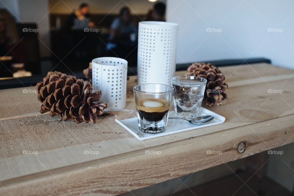 A glass of espresso sitting on a white plate next to a bubbly water in a fall season type theme. 