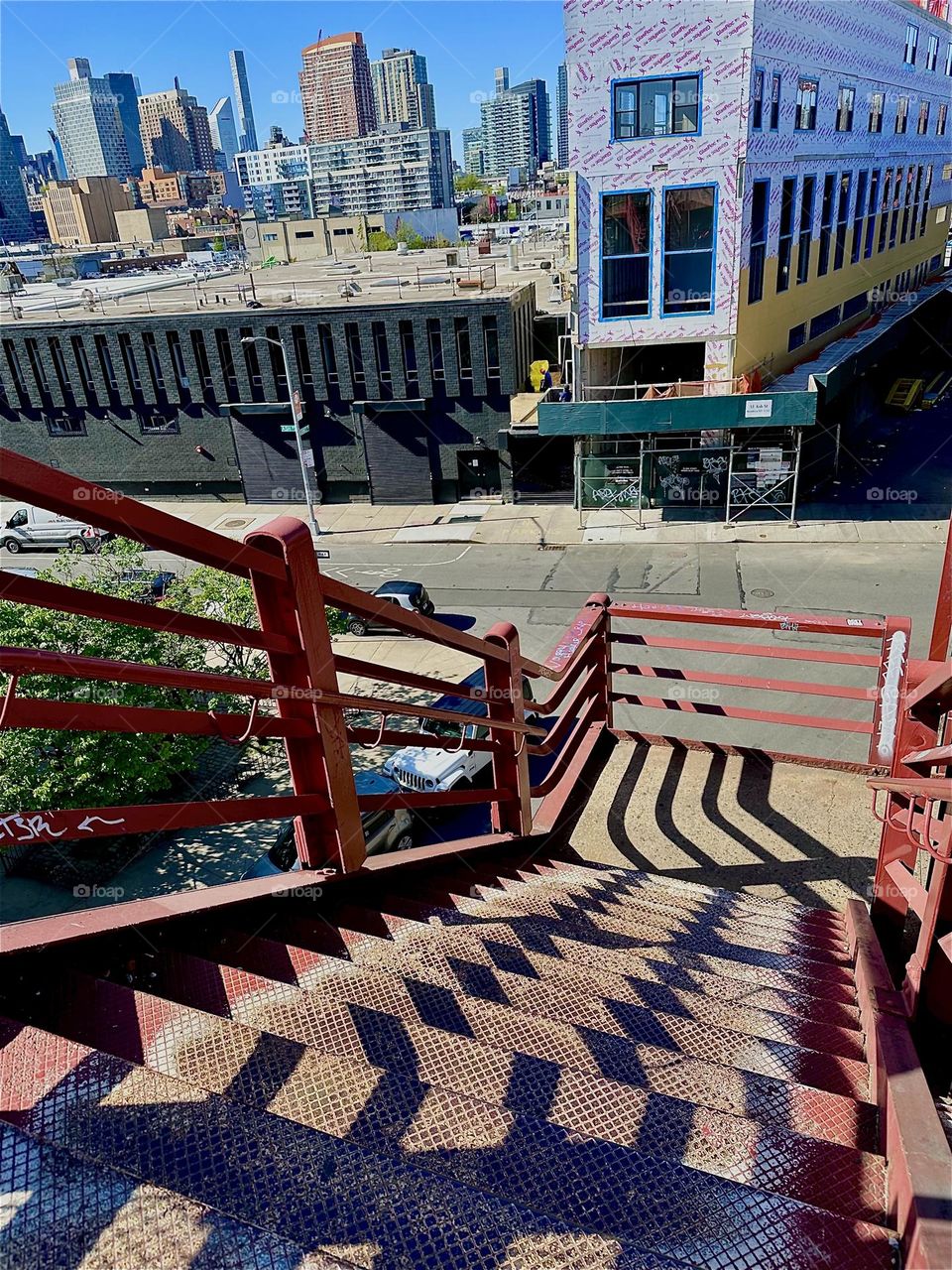 The red metal staircase of the “Pulaski Bridge” at “Newtown Creek” in “Greenpoint”, Bklyn has strong geometric elements. When the sun casts shadows onto its structures they combine to create intricate multifaceted patterns. 2024. Hypnotic Productions