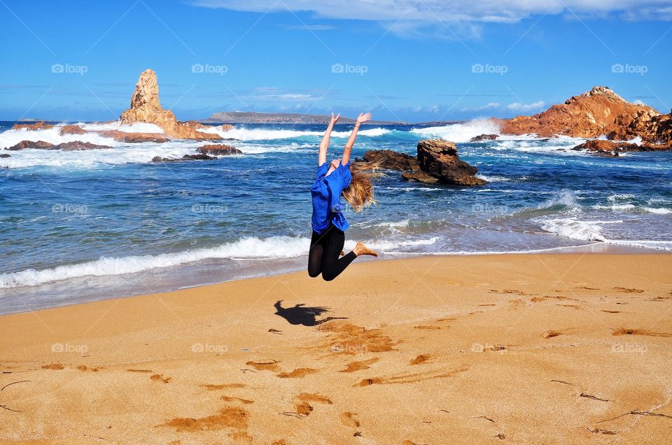 girl jumping on pregonda beach on menorca Balearic island in Spain