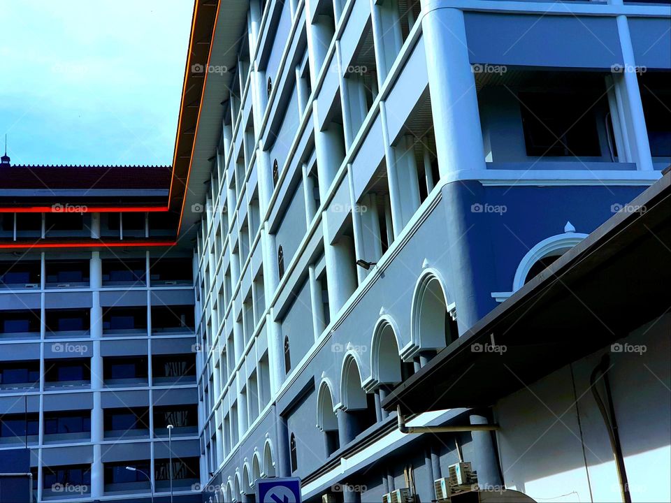 Office building in the city center, building owned by official government company, building with a modern classic motif, a magnificent front view with straight lines and curved lines, the building paint is light gray combined with dark gray