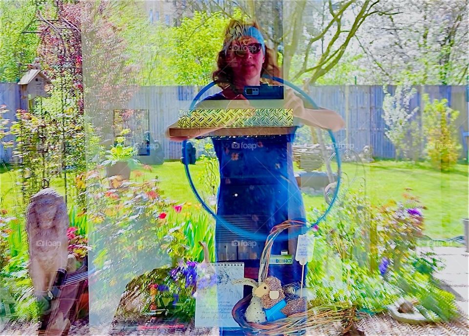 This exposure shows strong reflections in a window mirroring a beautiful garden in “Bavaria”, Germany with lush green grass, trees and blooming flowers as heralds of Spring. The room inside can only partially be seen. 2024. Hypnotic Productions