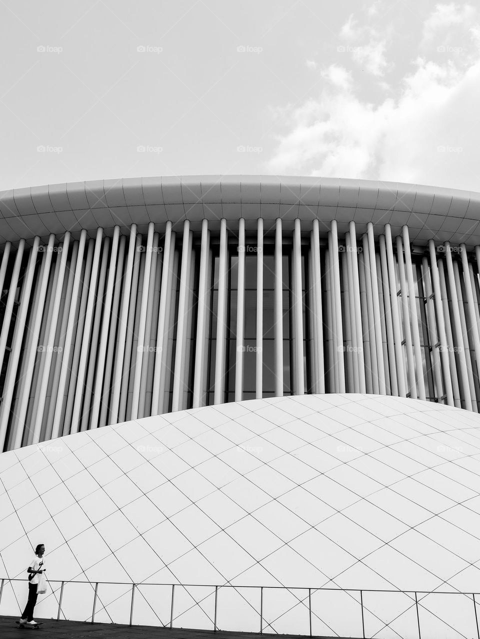 Beautiful view of the modern glass creative geometric lined building of the Philharmonic Hall with a blurry man riding a skateboard next to him, close-up side view. Concept architecture of modern buildings.