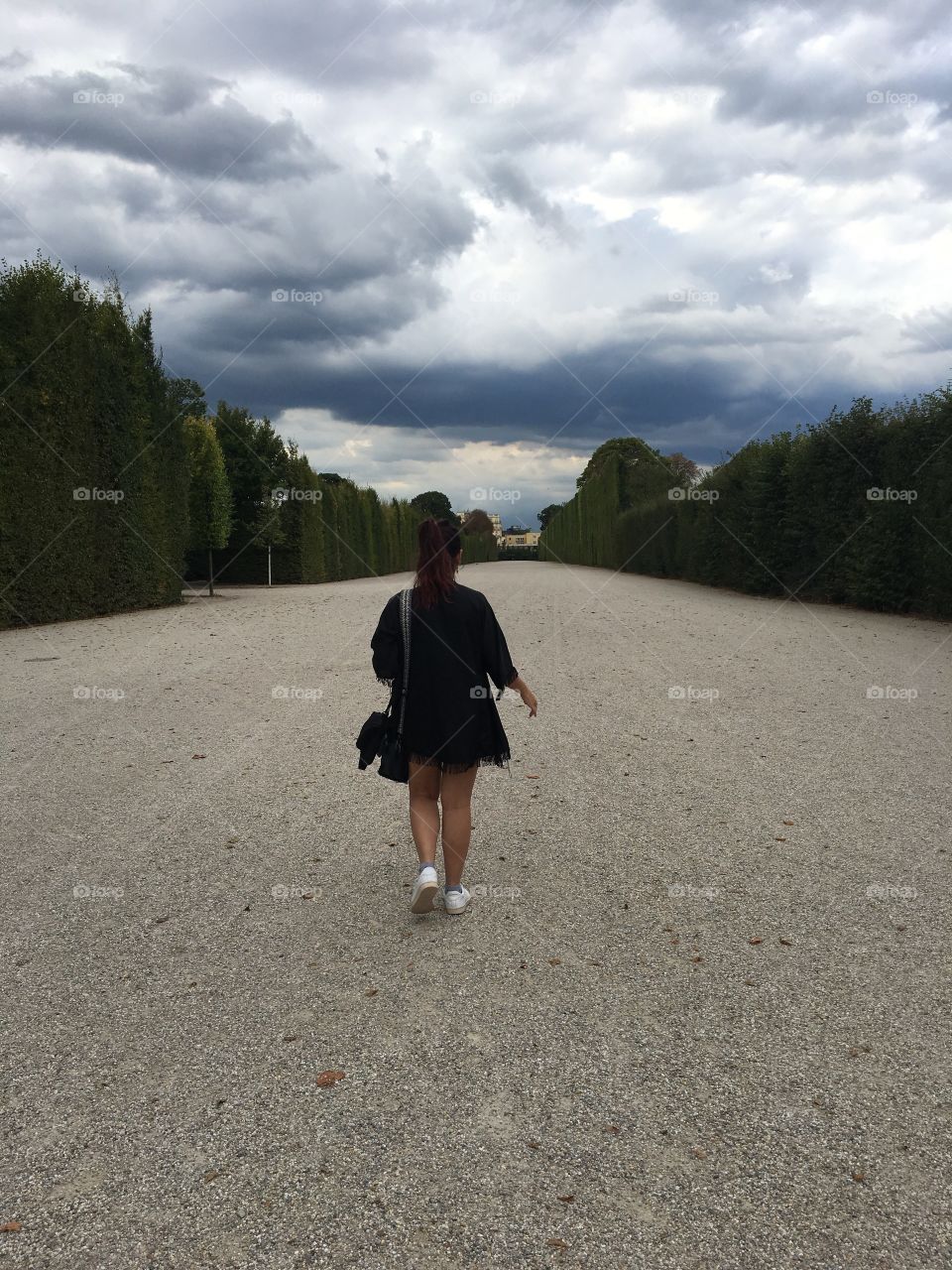 A woman walking along a wide path with trees all around 