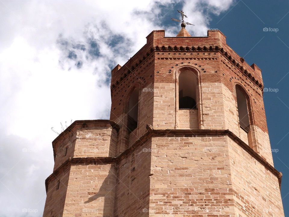 bell tower of a spanish gothic church, blue sky and white clouds.