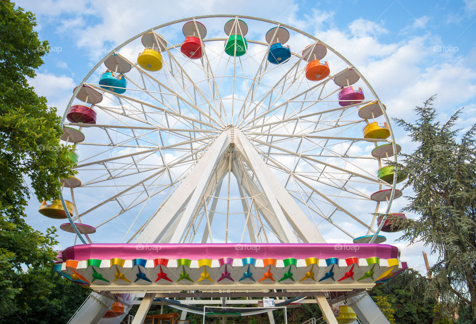 Amusement park colorful ferris wheel. Blue sky with clouds in the background.