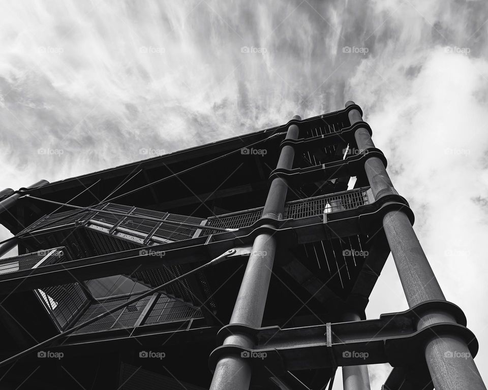 Black and white high angle view of a part of a building with high pillars and stairs in front of a cloudy sky