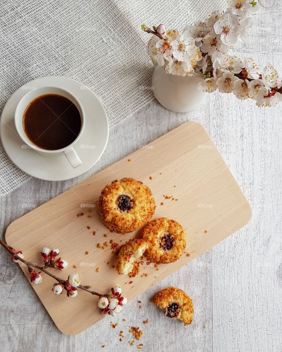 Homemade cookies with nuts and jam on the table near the cup with black coffee and some flowers. Top view.