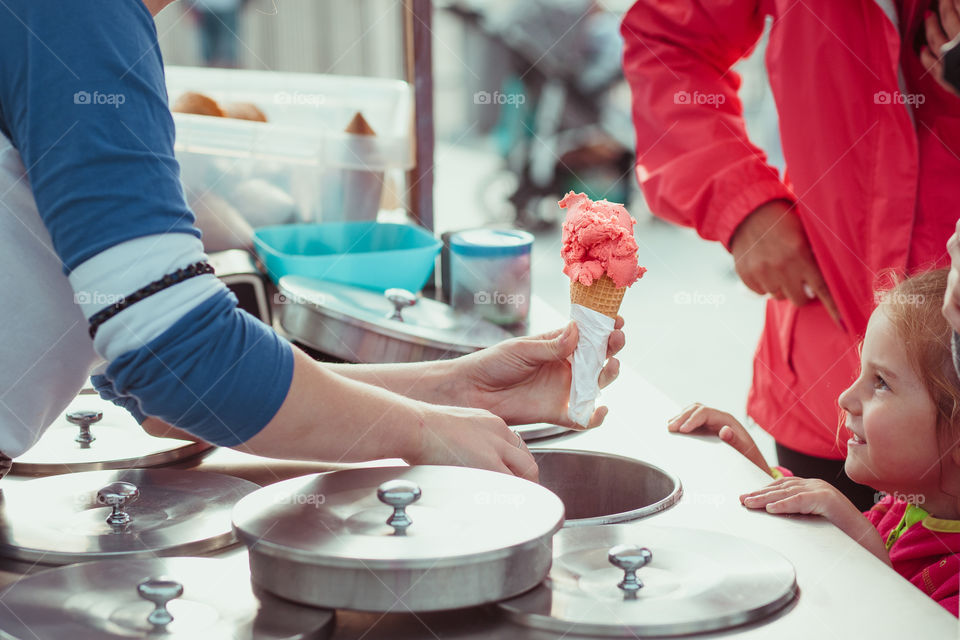 Little girl waiting for icecream. Mom buying a icecream her little daughter in a candy shop by the street. Young woman putting a scoop of pink icecream to a cone