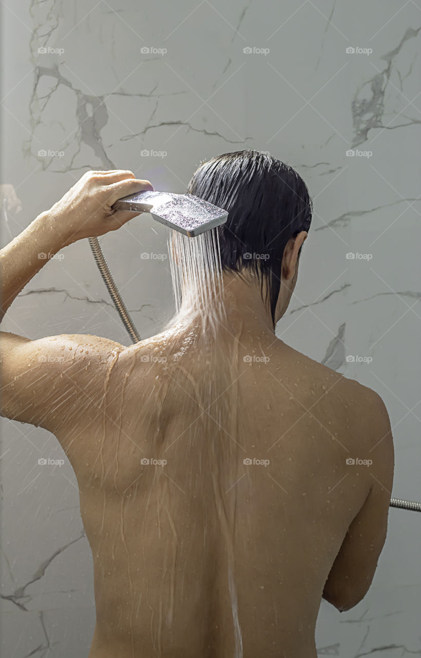 Asian man taking a shower in the bathroom.