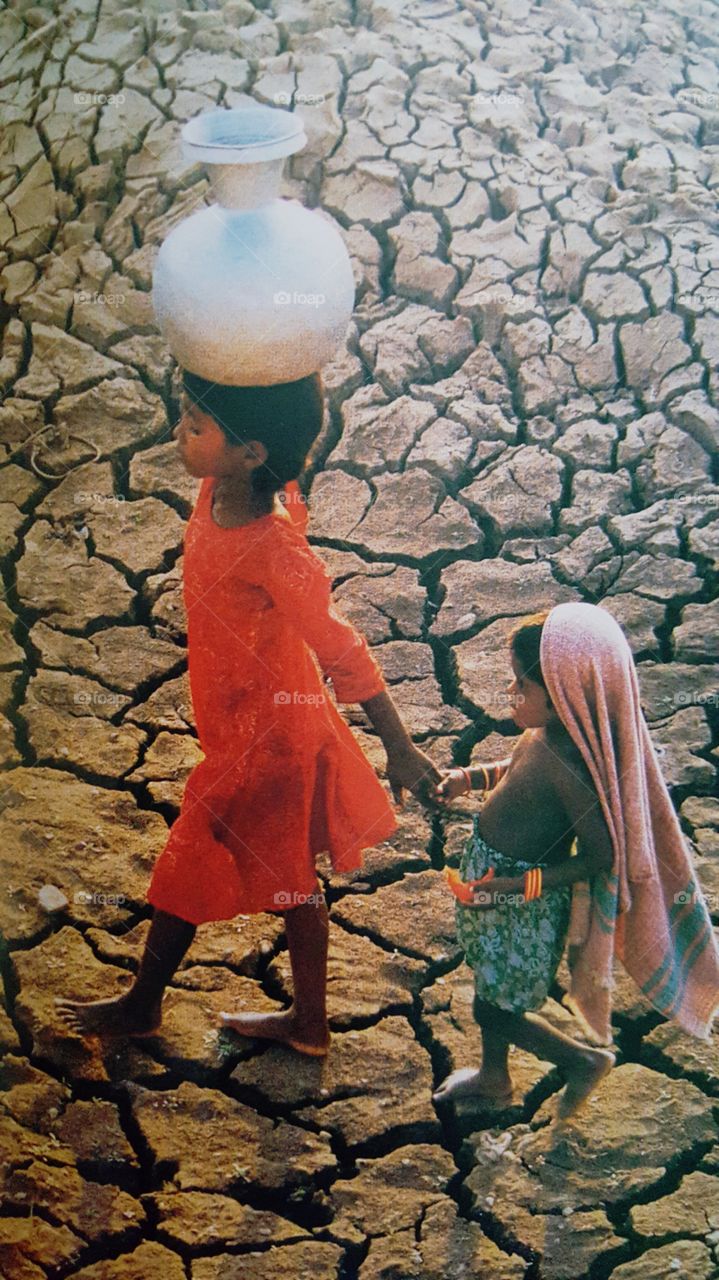 Girl with her sister carrying water container on her head