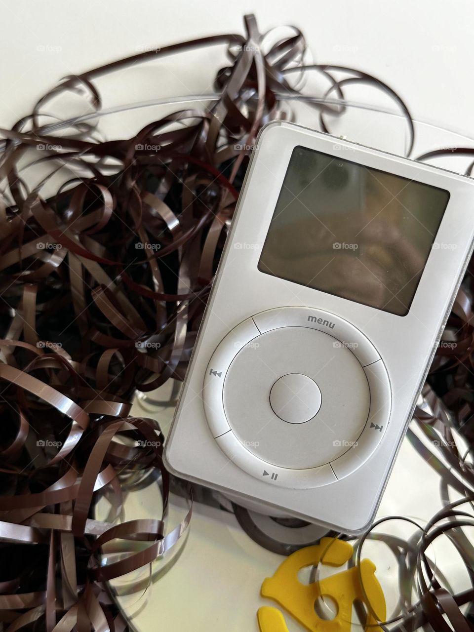 iPhone 14 Pro in original iPod screen reflection as it sits above a 33 RPM record among a tangle of audio cassette tape set on a CD with a yellow plastic 45 RPM record center spacer