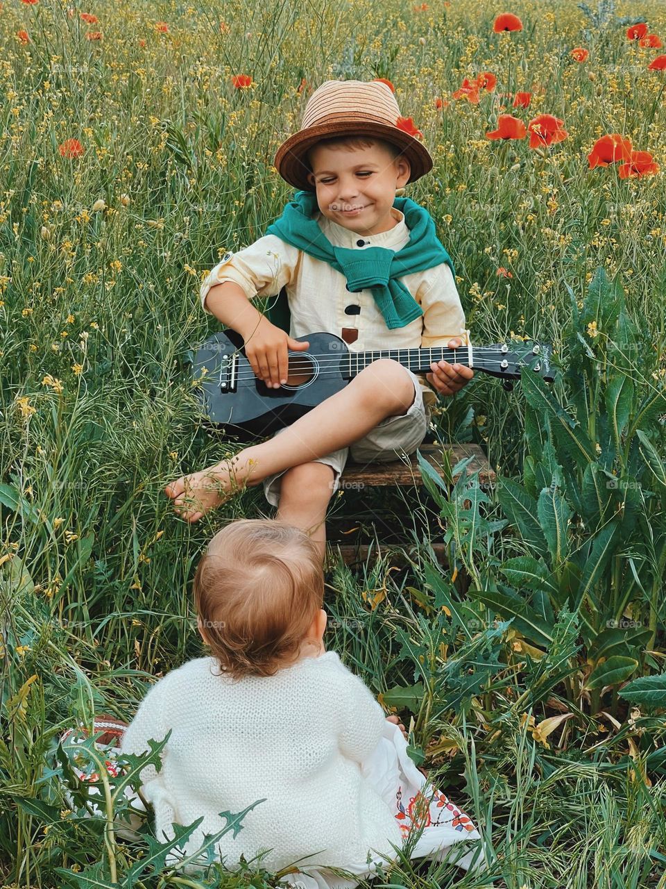 A toddler playing on guitar and his sister listening him with love♥️