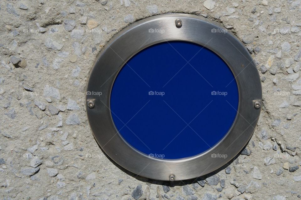 A recessed  lamp with a blue lens in a concrete wall at the Newtown Creek Park in  New York City.