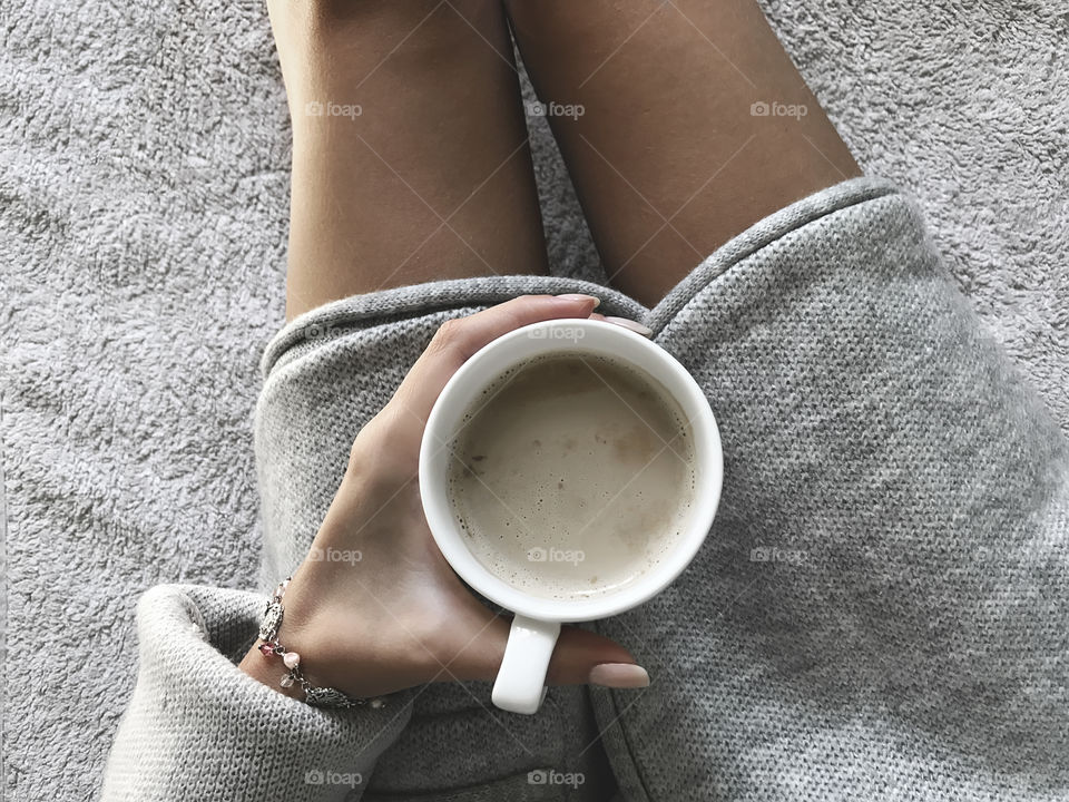 Young woman wearing cozy sweater enjoying coffee in cozy bed 