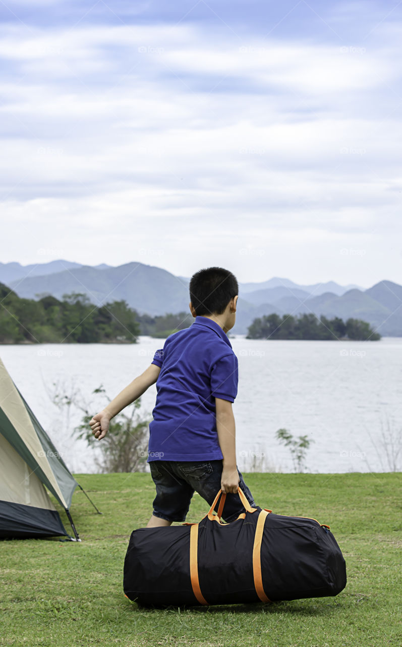 Asian boy holding Backpack tent Background grass and water at Kaeng Krachan Dam ,Phetchaburi in Thailand.