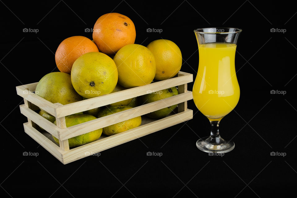 Fruit box with oranges and crystal glass with juice on black background