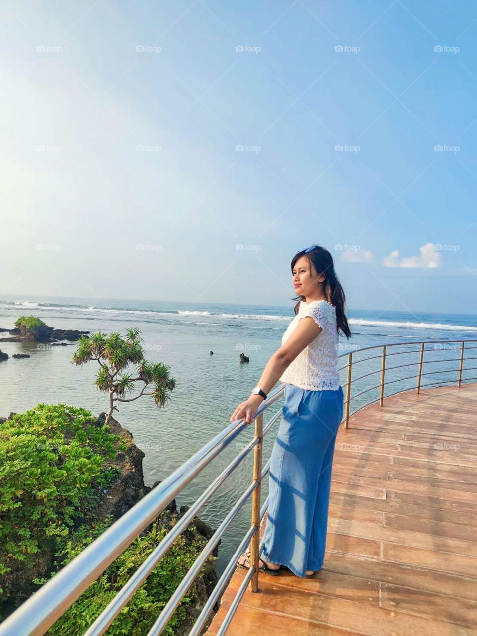 Portrait of a young woman standing on the railing looking at the beautiful sea view with a clear sky