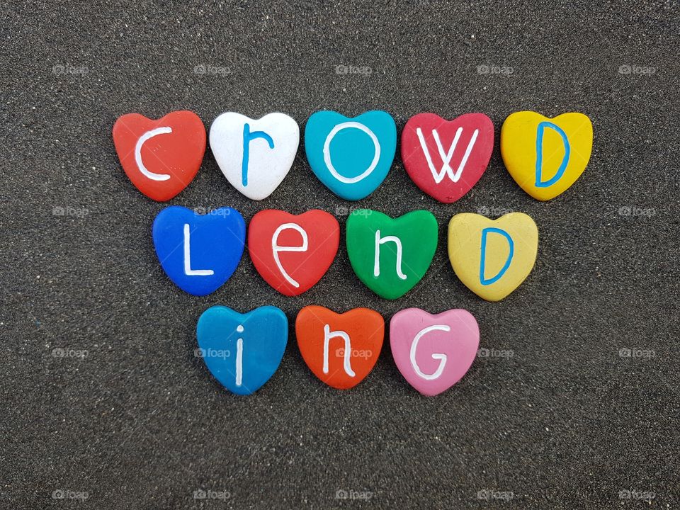 Crowdlending text with multicolored heart stones over black volcanic sand