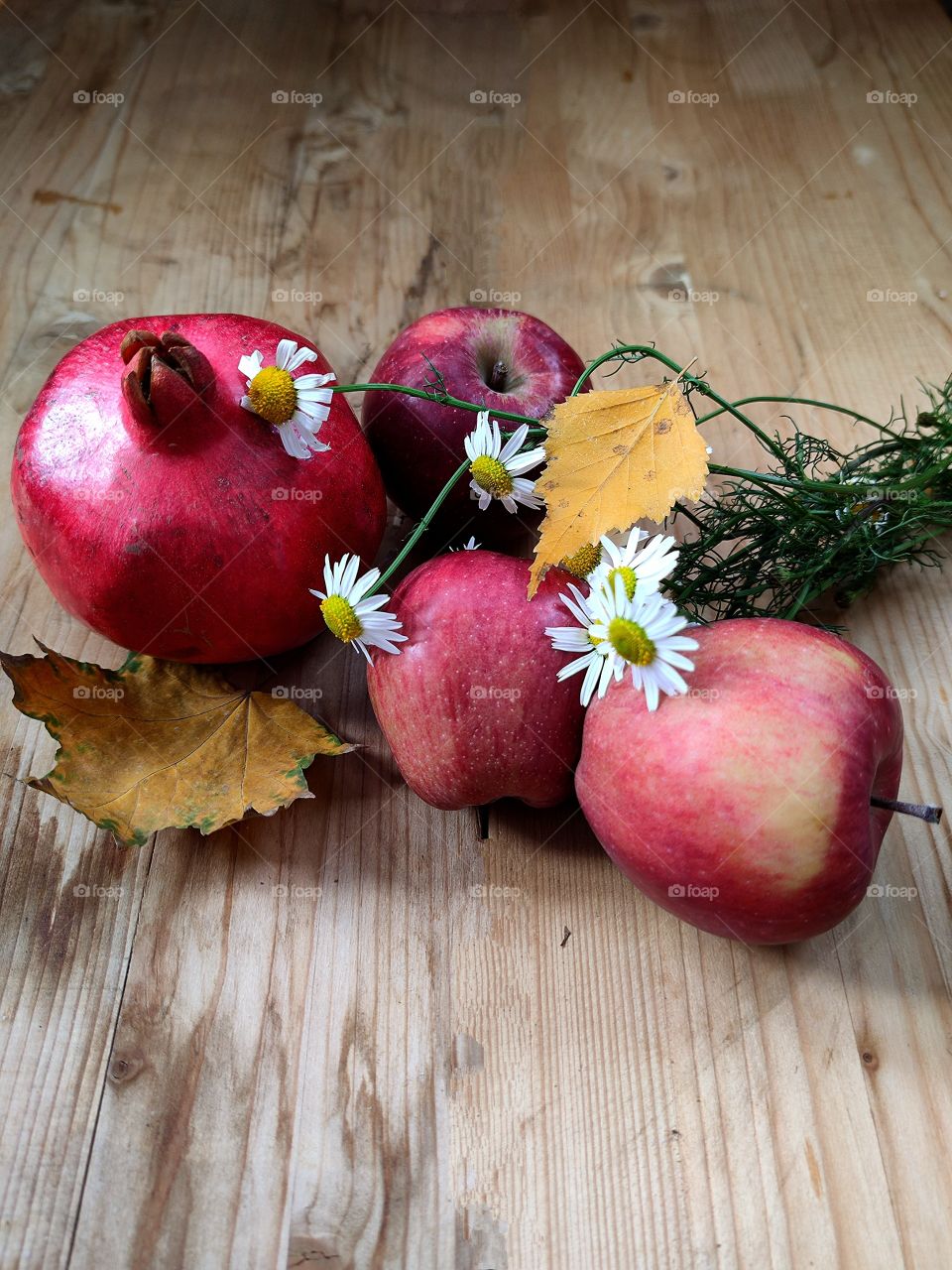 Autumn composition.  Red pomegranate, three red apples, a bouquet of daisies and yellow leaves