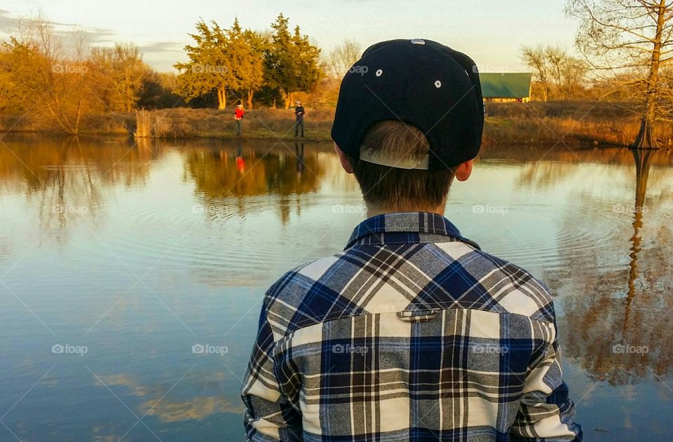 Three boys men enjoying fishing in a pond on a beautiful fall winter day with reflection across the water one close with baseball cap two on far shore