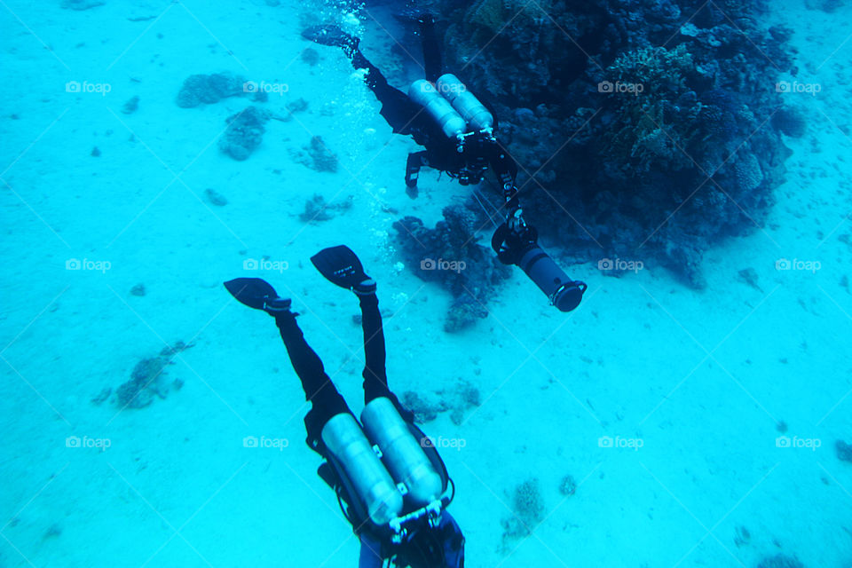 Two people diving in the blue water of the sea with corals 