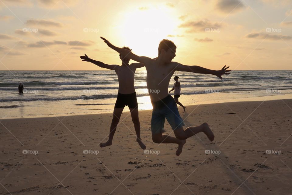 Kids jumping making fun stunts on the beach during sunset 