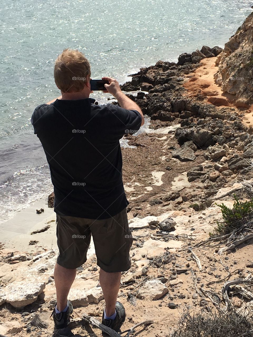 Back view man photographing ocean cliffs from cliff