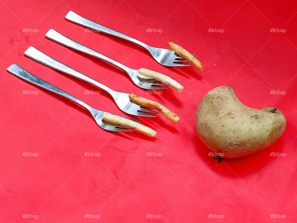 A heart-shaped potato with four metal forks next to it.  On each fork is a straw of french fries.  red background