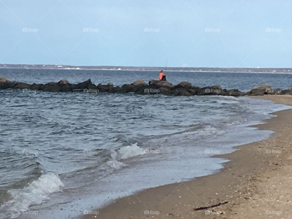 Fisherman fishing on a rocky pier on the beach.