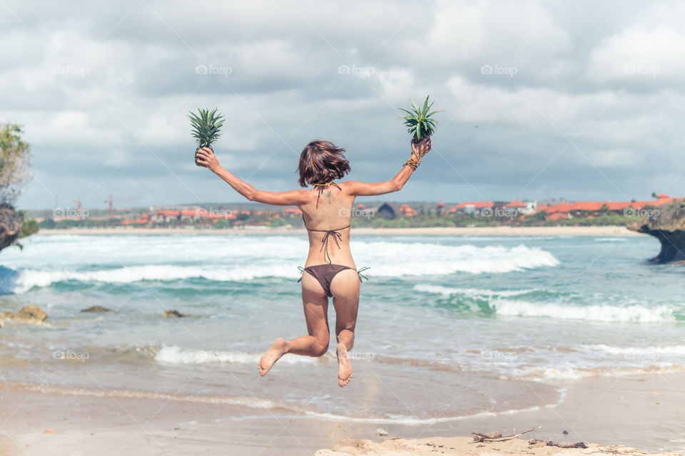 Girl jumping on the beach, in the hands of pineapples. Bali island. Nusa-Dua.