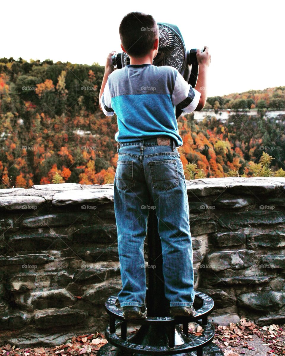 Boy looking through binoculars at landscape in fall. 