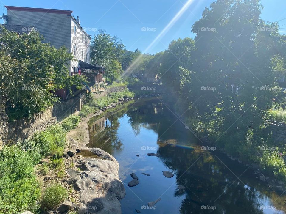 Looking from a bridge over the river lined with plants and flowers in a quant New England town on a sunny summer afternoon. 