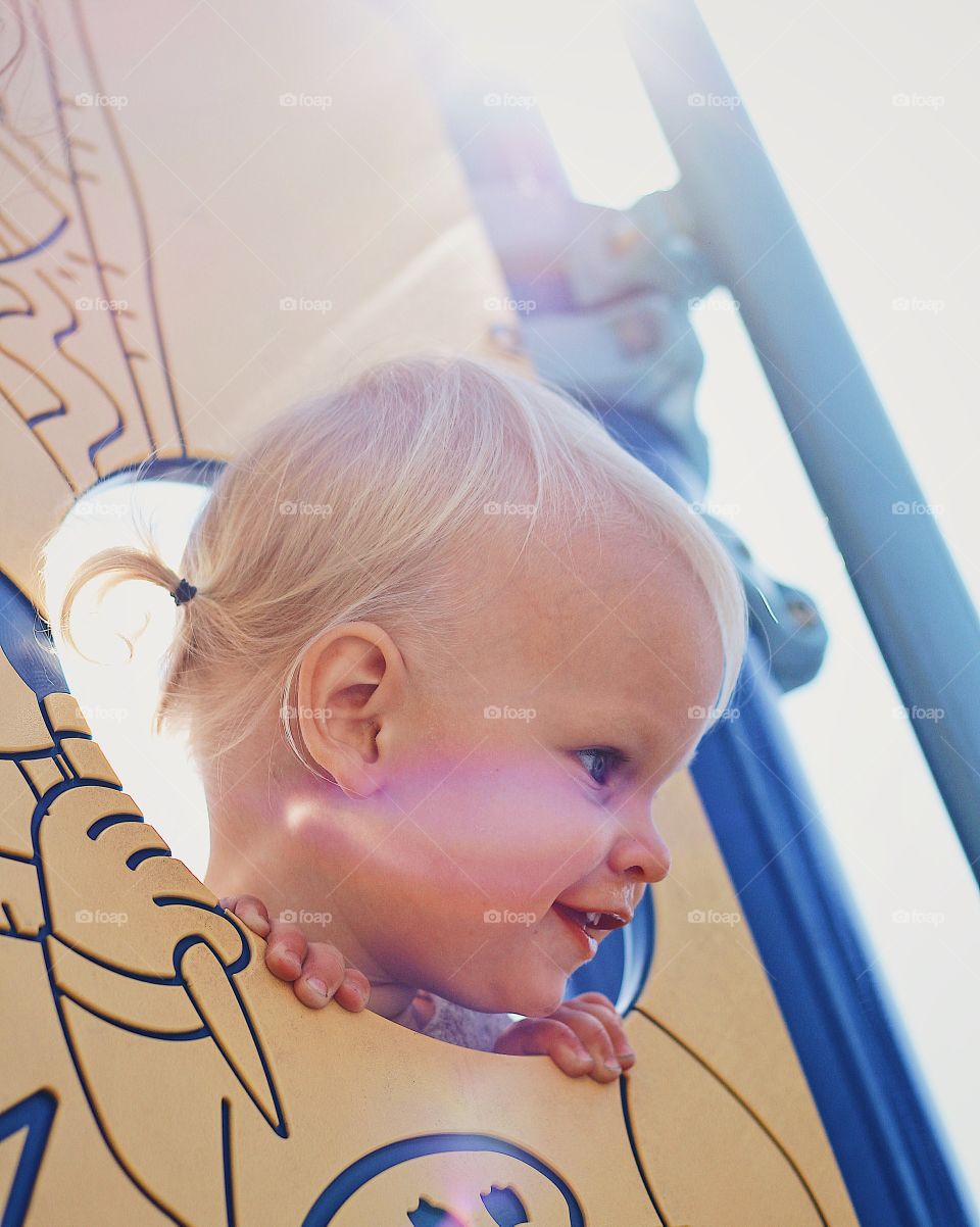 Beautiful baby girl playing peek a boo at a park with shining sun