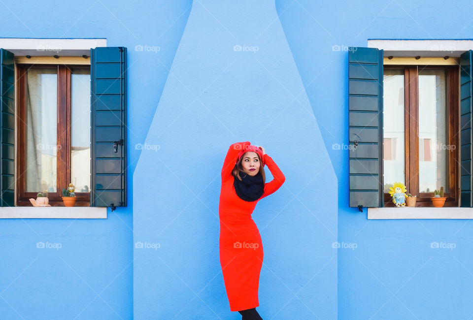 Attractive Asian woman in red dress on bright blue wall background 