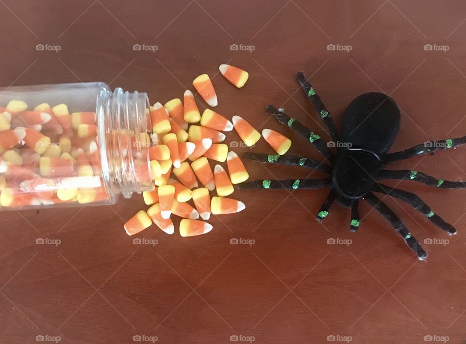 A display of a black spider sitting next to a glass jar of spilled candy corns. Happy Halloween 