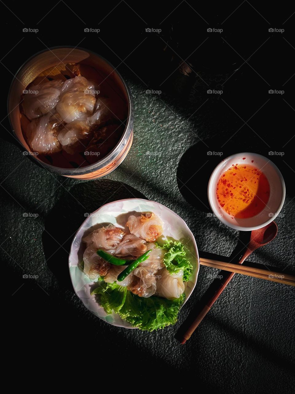 Round shape plate with crystal shrimps dumplings on it and spicy sauce in a round plate beside it
