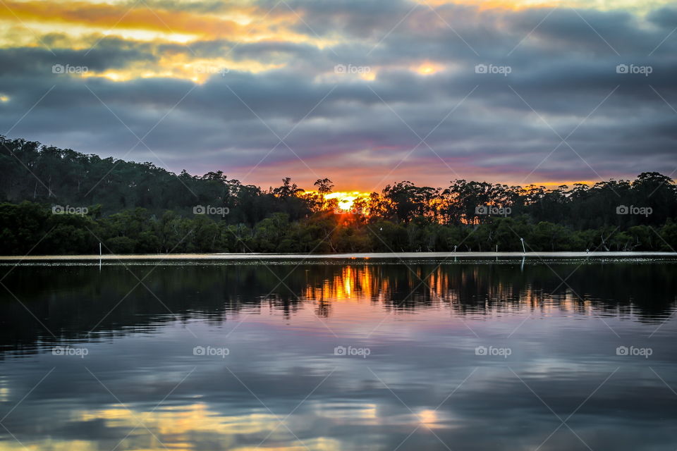 Cloudy sunrise reflected in river surrounded by trees