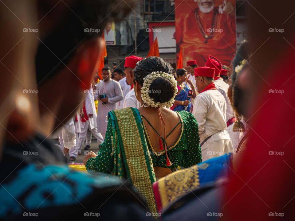 A photo of a traditionally dressed beautiful woman playing dhol and has flower pinned in hair also known as gajra